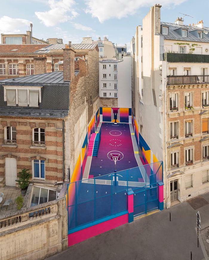 Colorful modern basketball court nestled between old European-style buildings showcasing old versus modern architecture contrast.
