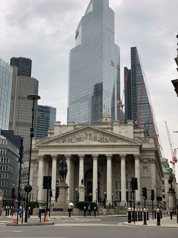 Historic classical building with columns contrasted against modern glass skyscrapers in a cityscape showing old versus modern architecture.