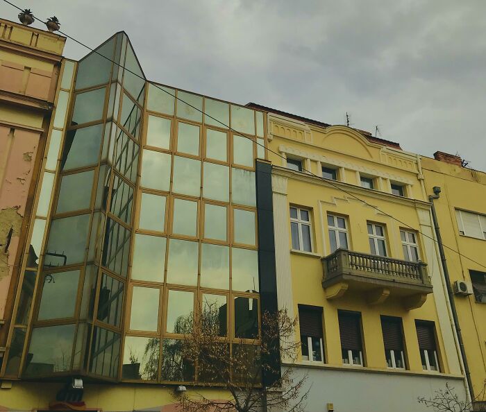 Old versus modern architecture showing a glass facade building next to a traditional yellow residential building.