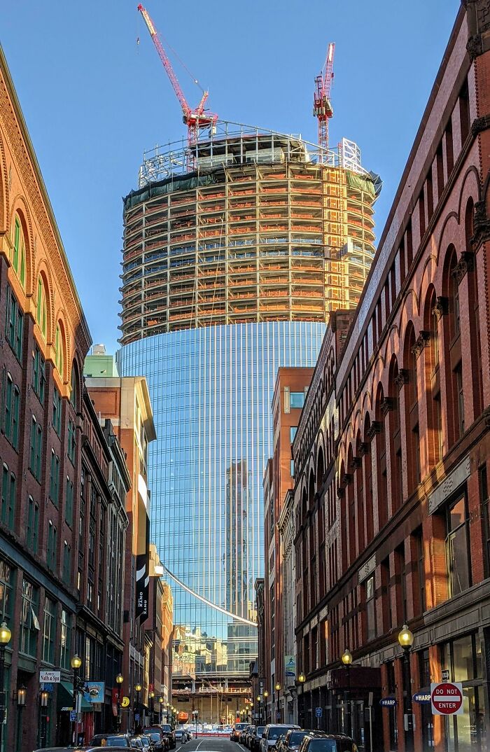 Modern glass skyscraper under construction contrasts with old brick buildings lining the street in old versus modern architecture.