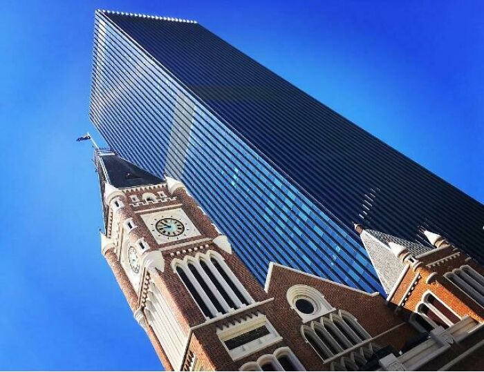 Old versus modern architecture shown with a historic clock tower in front of a sleek glass skyscraper under a clear blue sky.