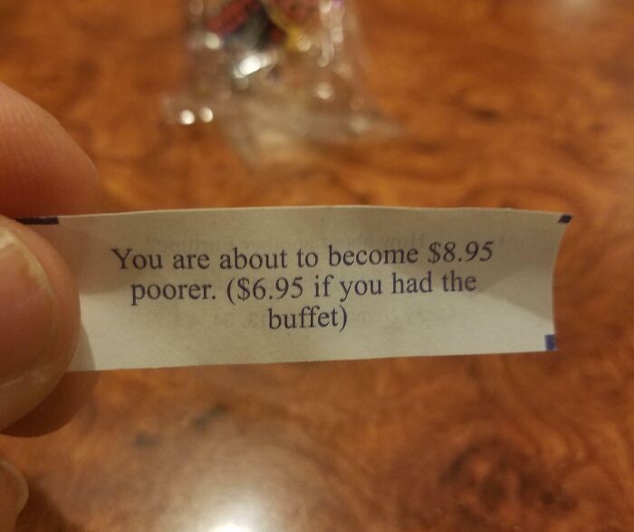 Hand holding a humorous fortune cookie slip about becoming poorer, illustrating random notes that lighten life.