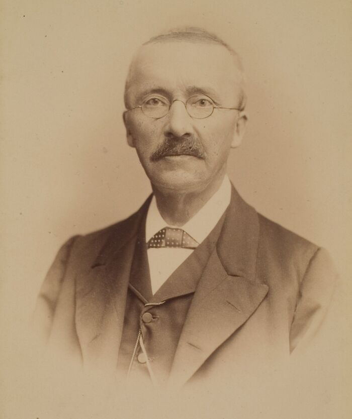 Portrait of an elderly man with glasses and mustache wearing a suit, representing savage roasts and comebacks.