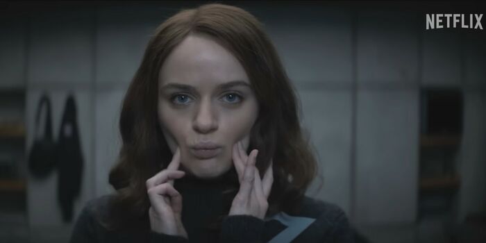 A woman with red hair in a dark sweater making a face in a dimly lit room, representing Netflix movies letdowns.