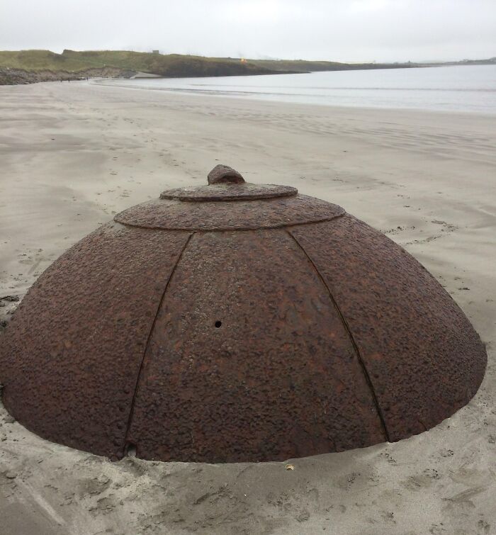 Rusty dome-shaped metal object partially buried in sand, one of the interesting and bizarre things found at the beach.
