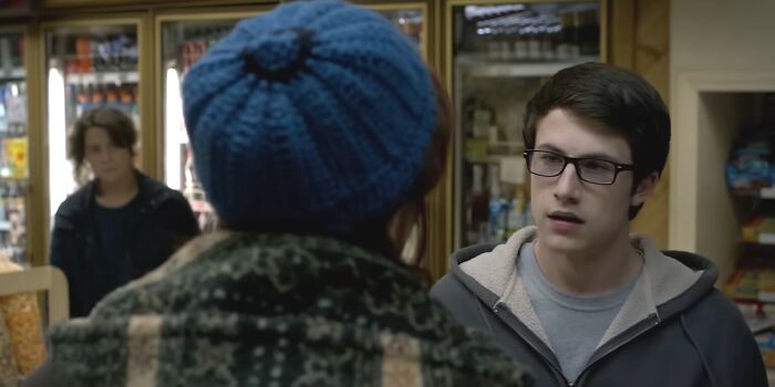 Young man wearing glasses talks to person in blue knit hat inside a small convenience store in Netflix movies letdowns scene.