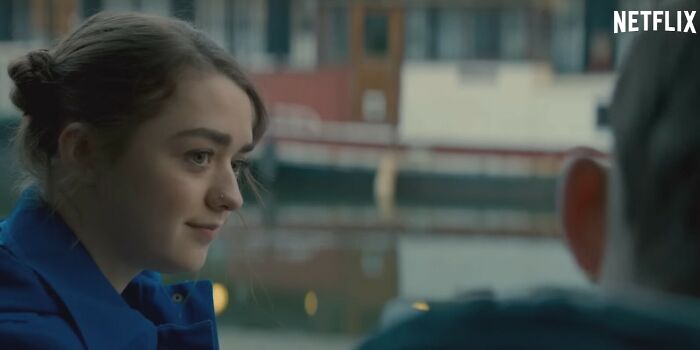 Young woman in a blue jacket having a conversation by the waterfront in a scene from Netflix movies letdowns.