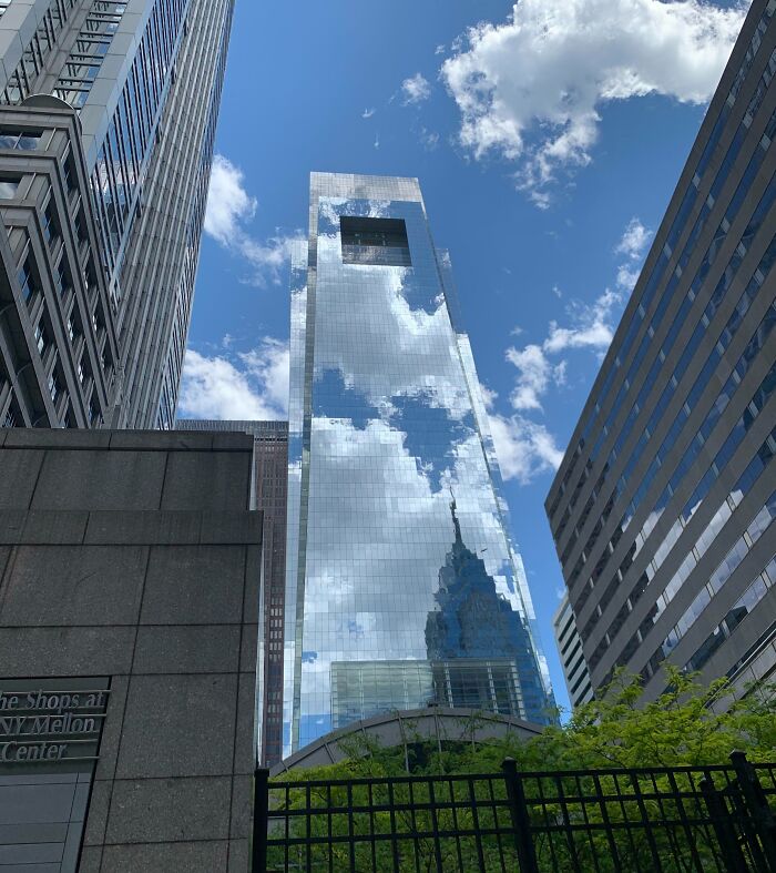 Reflective building perfectly matching its surroundings with clear blue sky and clouds blending into the glass facade.