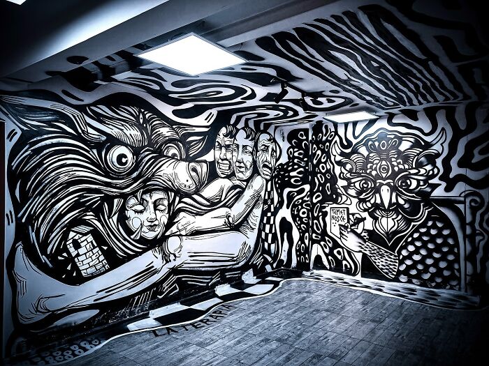 Black and white mural artwork by Colombian artist SakoAsko blending fantasy and reality in an indoor space with detailed figures.
