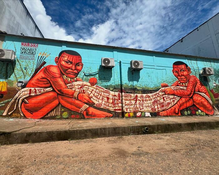 Mural by Colombian artist SakoAsko featuring vibrant red figures blending fantasy and reality on a large outdoor wall.
