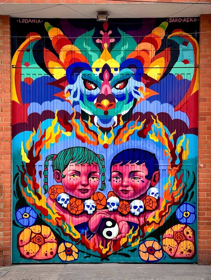 Colorful mural by Colombian artist SakoAsko featuring fantasy elements and two children surrounded by flames and skulls.