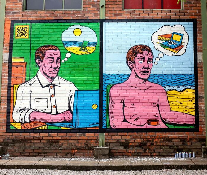 Mural by Colombian artist SakoAsko showing two men imagining beach and laptop scenes blending fantasy and reality.