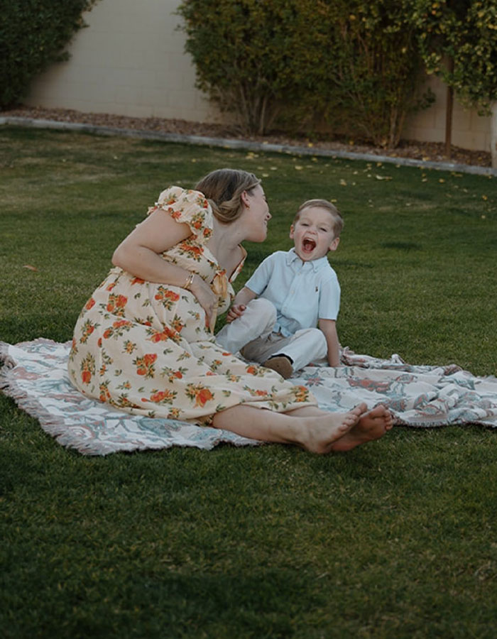 Mother and young child sitting on a blanket in grass, highlighting momfluencer taking accountability after tragic drowning incident. Mother and young child sitting on a blanket in grass, highlighting momfluencer taking accountability after tragic drowning incident.