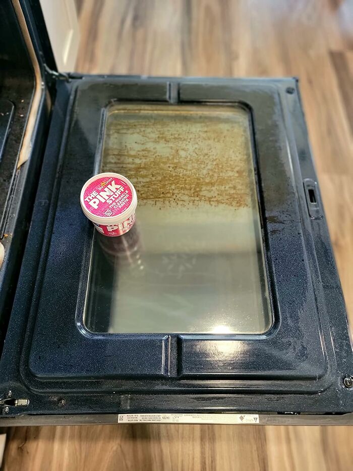 Oven door being cleaned with a tub of The Pink Stuff, demonstrating genius cleaning tricks for impressing in-laws.