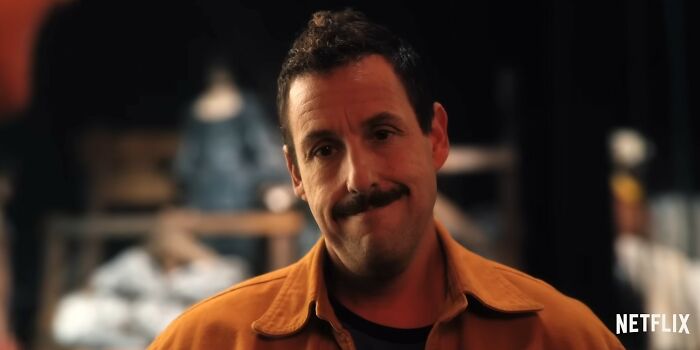 Actor Adam Sandler with a mustache wearing a brown jacket in a scene from a Netflix movie letdown.