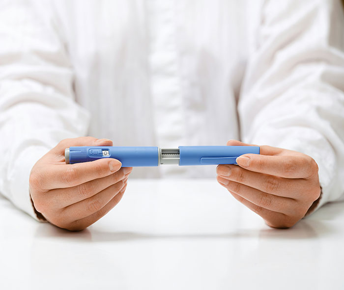 Hands holding a blue medical injector pen related to Ozempic vulva side effects from weight-loss medication use. Hands holding a blue medical injector pen related to Ozempic vulva side effects from weight-loss medication use.