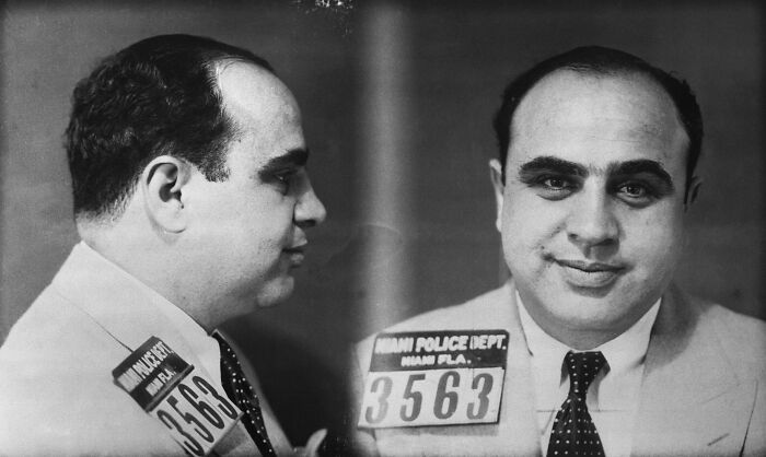 Black and white mugshot of a notorious mob boss wearing a suit and tie with Miami Police Department badge visible.