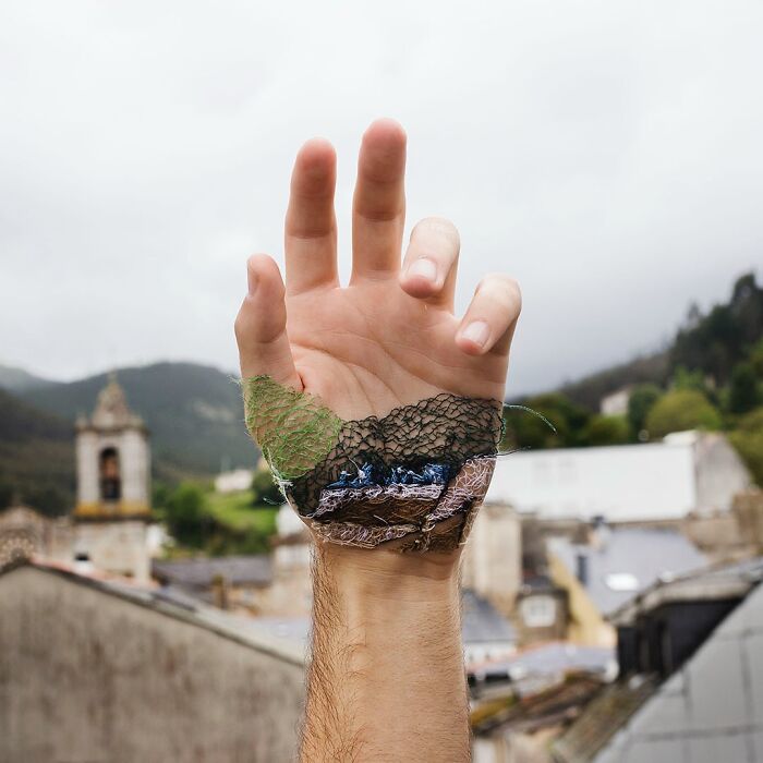 Hand with a stitched landscape artwork on skin showing mountains, trees, and sky in detailed embroidery.