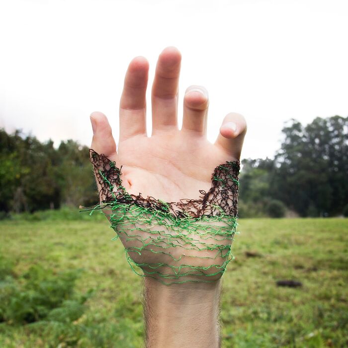 A hand with intricate landscape stitching on skin, blending green and brown threads to mimic nature.