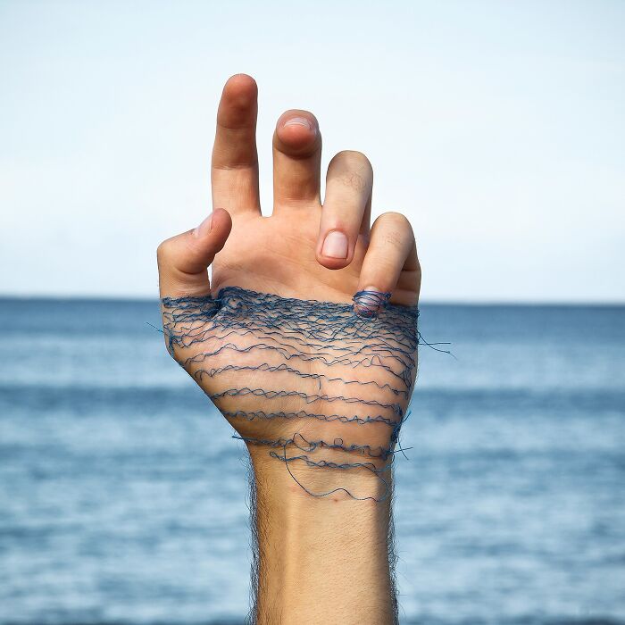 Hand with blue thread stitching creating a landscape effect on skin, blending art and nature by stitching landscapes onto skin.