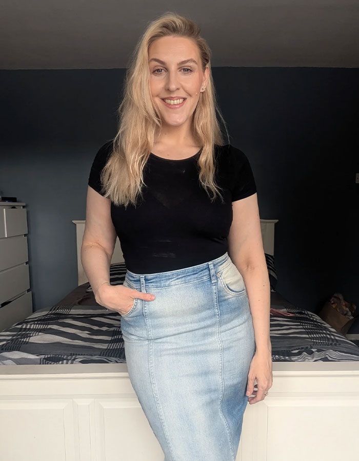 Smiling woman standing in a bedroom wearing a black top and denim skirt, relating to passenger sharing worst experience with child on flight. Smiling woman standing in a bedroom wearing a black top and denim skirt, relating to passenger sharing worst experience with child on flight.