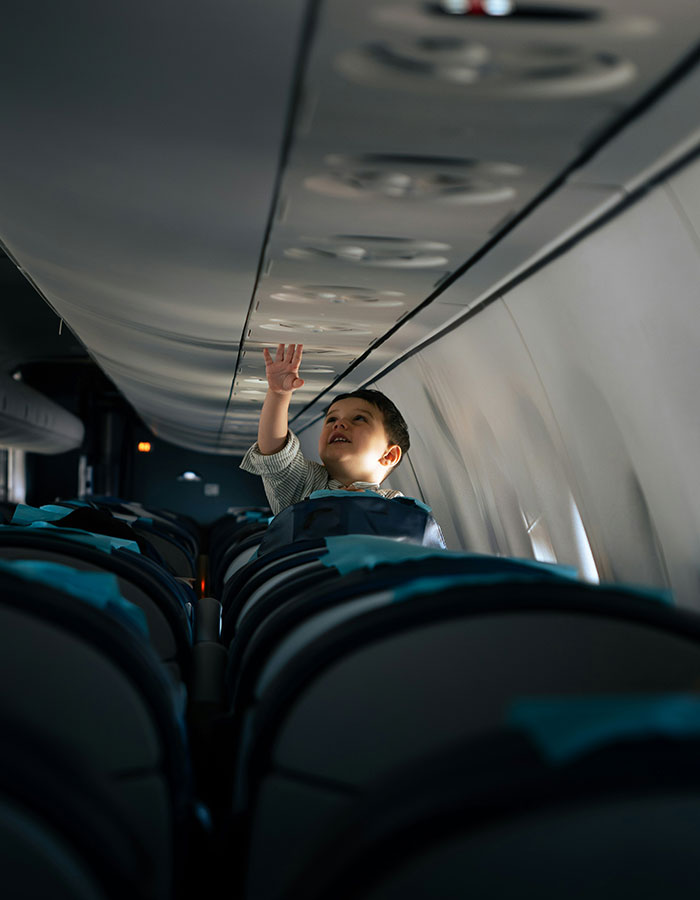 Child on flight reaching overhead compartment, highlighting passenger experience with bored child sparking debate on plane journey. Child on flight reaching overhead compartment, highlighting passenger experience with bored child sparking debate on plane journey.