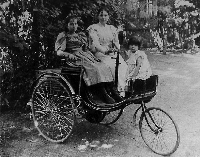 Three young girls seated in a wild first car from 100 years ago, showcasing early automobile design and style.