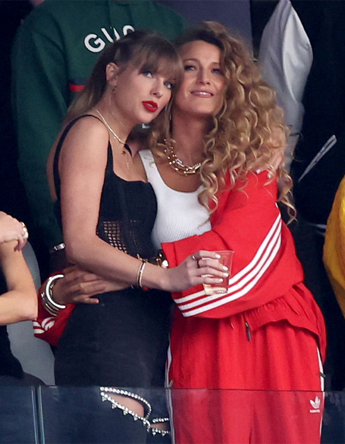 Blake Lively in red outfit hugging a woman in black dress, related to leading role in new rom-com controversy. Blake Lively in red outfit hugging a woman in black dress, related to leading role in new rom-com controversy.