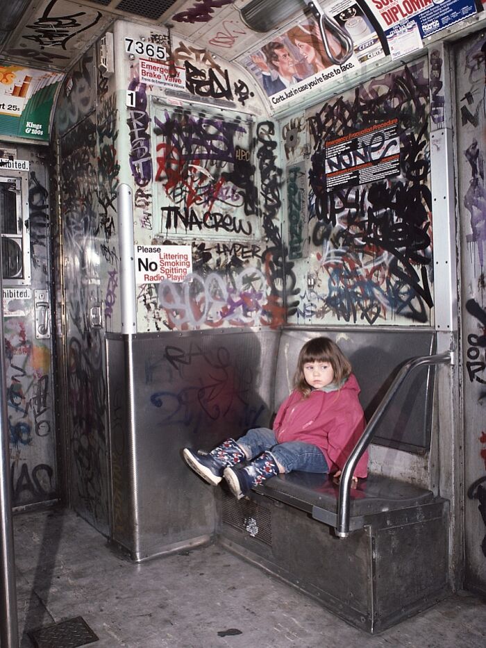 Young girl in pink coat sitting alone on a graffiti-covered subway train, showcasing historical photos with striking backstories.