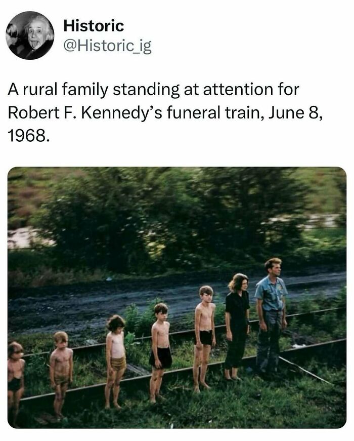 Rural family standing at attention by railroad tracks during Robert F. Kennedy funeral train in historic photo.