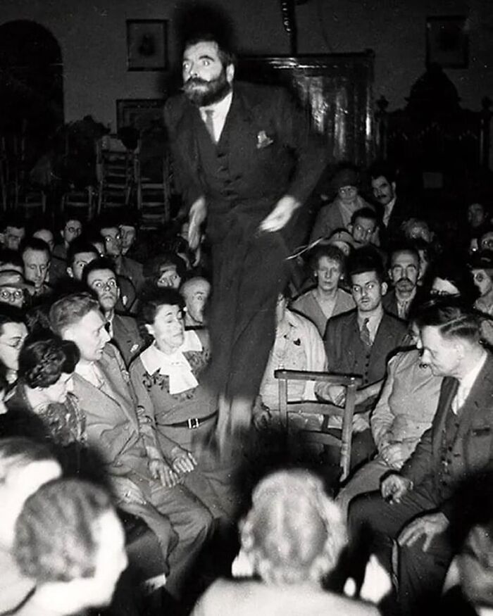 Black and white historical photo of a man jumping in the middle of a seated crowd showing an interesting moment in history.
