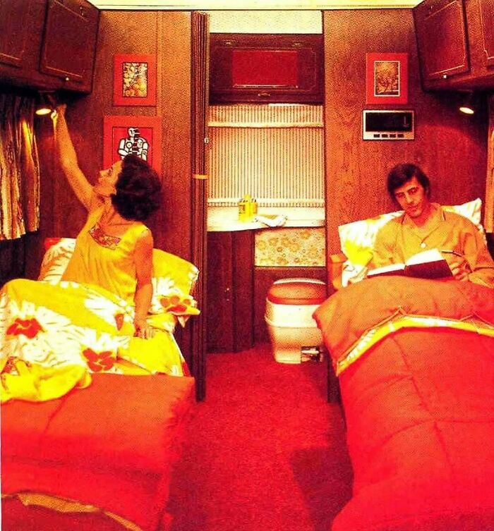 Couple in a vintage camper bedroom with floral bedding and wood paneling, evoking June Cleavers vintage closet style.