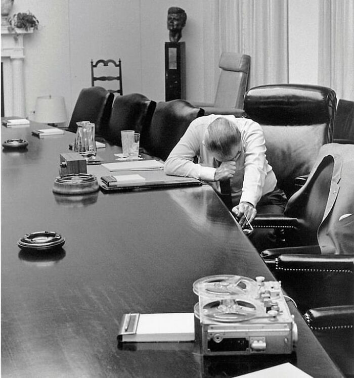 Man sitting at a long conference table with head bowed in a tense moment captured in historical photos backstories.