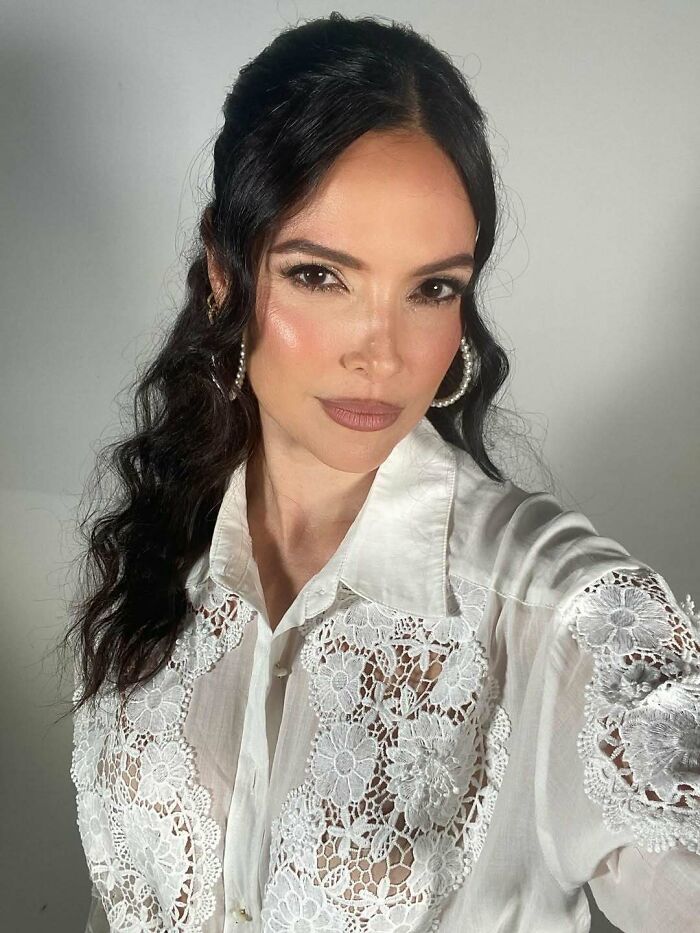 Miss Universe winner posing for a close-up photo wearing a white lace blouse and hoop earrings with natural makeup.