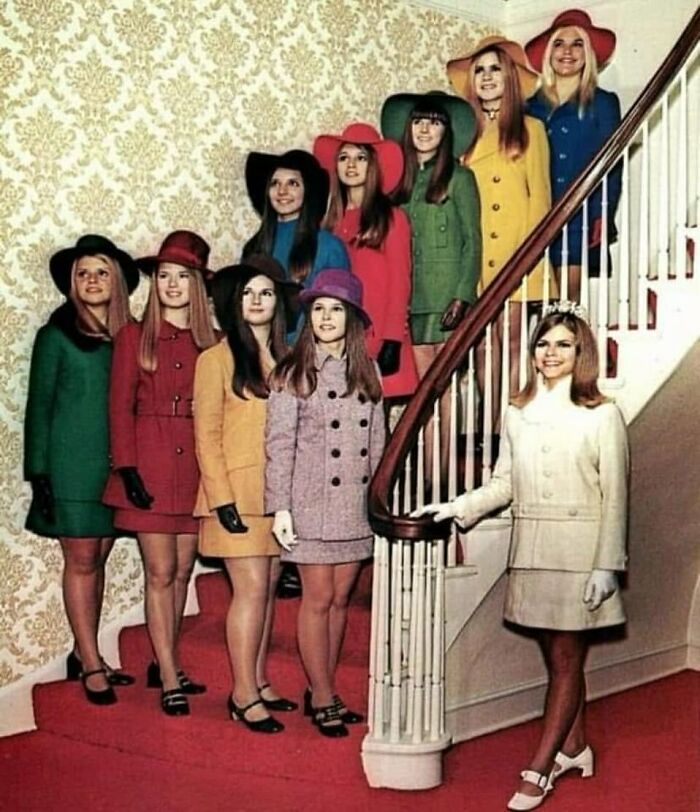 Group of women dressed in vintage 1960s-style colorful coats and hats on a staircase, evoking June Cleavers vintage closet.