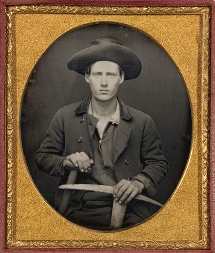 Black and white historical photo of a young man wearing a hat, holding a tool, with an interesting backstory.