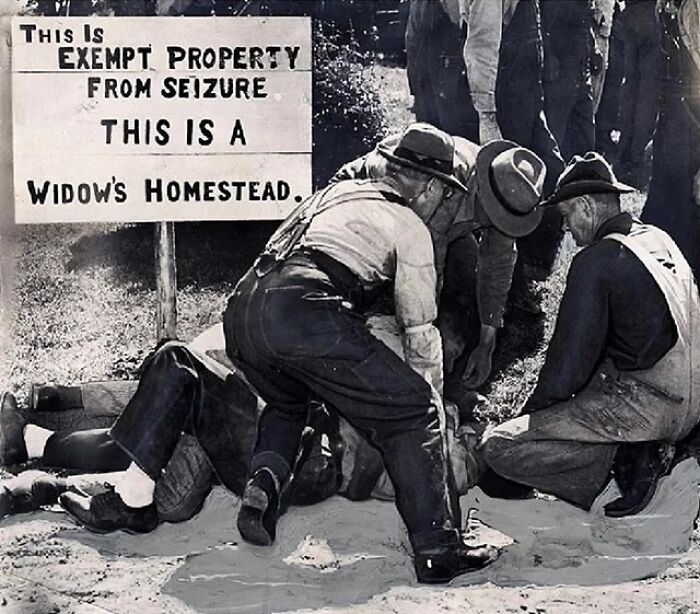 Group of men digging near a sign claiming exempt property on a widow’s homestead in a historical black and white photo