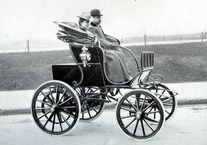 Vintage black early car with two passengers seated, showcasing how wild the first cars really were 100 years ago.