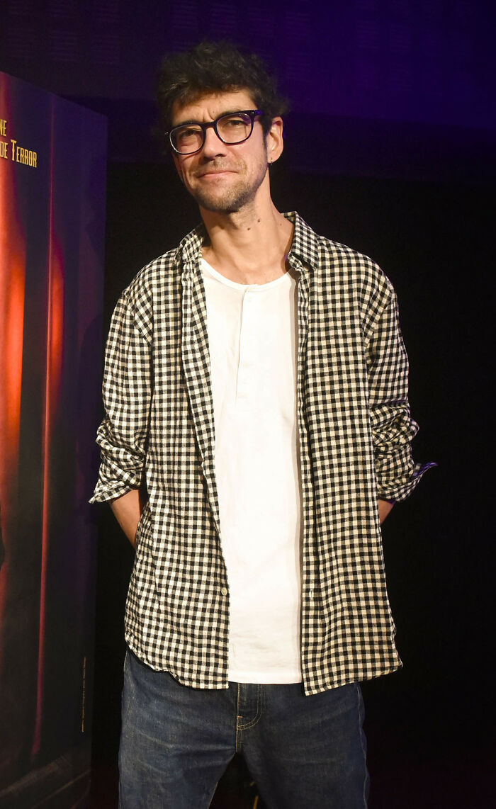 Man wearing glasses and a checkered shirt standing in a dimly lit room, representing proof that superhumans walk among us.