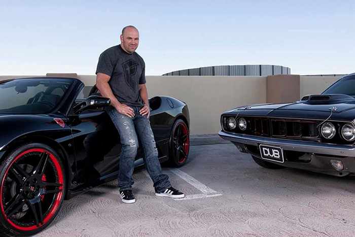 Dana White leaning on a black sports car in a parking lot, showcasing luxury and rising net worth with UFC events. Dana White leaning on a black sports car in a parking lot, showcasing luxury and rising net worth with UFC events.