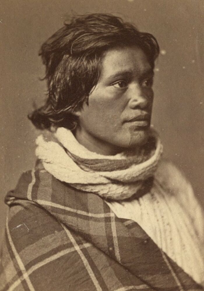 Sepia portrait of Māori man wearing traditional cloak and scarf, representing Māori life a century ago.