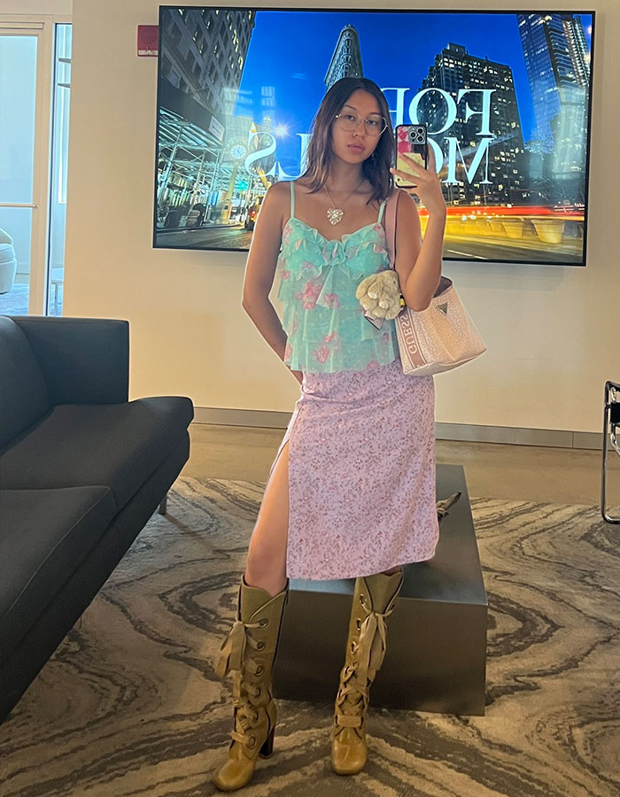 Gen Z worker posing in trendy office attire with floral top, pink skirt, and brown lace-up boots supporting workplace dress code debate. Gen Z worker posing in trendy office attire with floral top, pink skirt, and brown lace-up boots supporting workplace dress code debate.