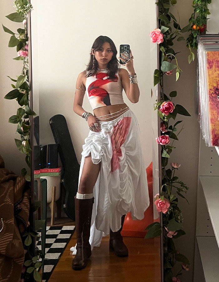 Gen Z worker takes mirror selfie wearing edgy office dress code outfit with boots and accessories in bedroom decorated with flowers. Gen Z worker takes mirror selfie wearing edgy office dress code outfit with boots and accessories in bedroom decorated with flowers.