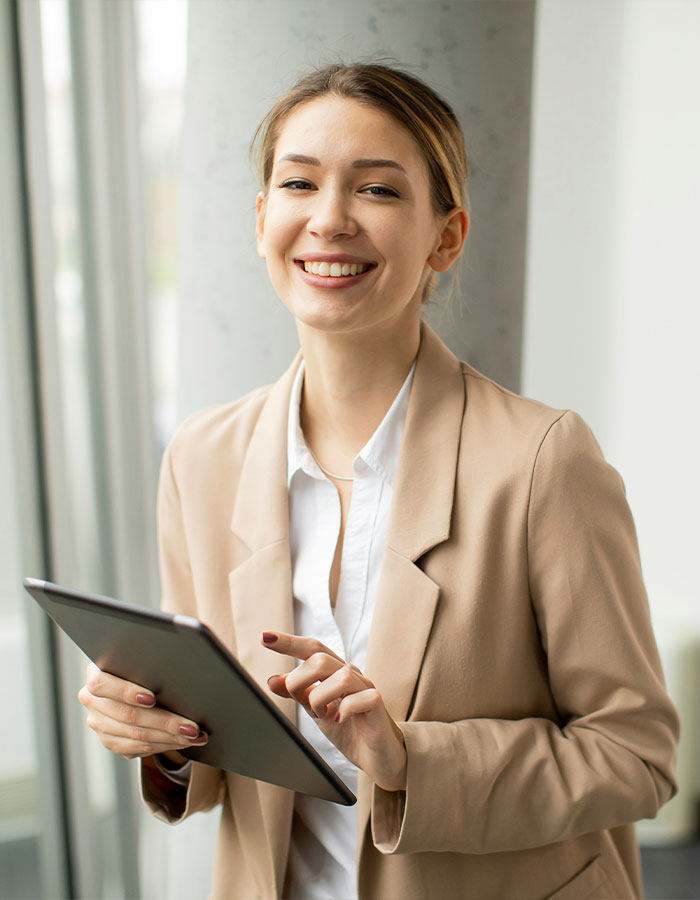 Young Gen Z worker in beige blazer smiling while using a tablet, representing office dress code debate and netizen defense. Young Gen Z worker in beige blazer smiling while using a tablet, representing office dress code debate and netizen defense.