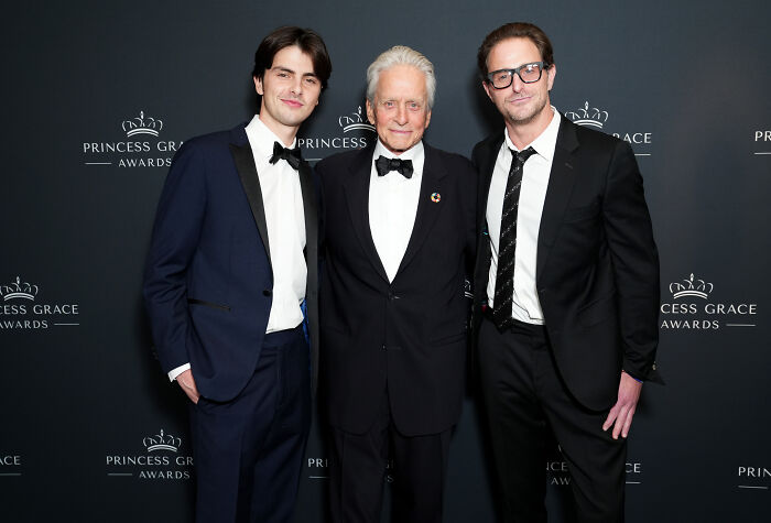 Three men dressed in formal black tuxedos posing together at the Princess Grace Awards, representing legendary entertainment families.