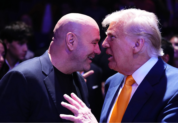 Dana White in a dark suit smiling and speaking closely with a man in a blue suit and orange tie at a UFC event. Dana White in a dark suit smiling and speaking closely with a man in a blue suit and orange tie at a UFC event.