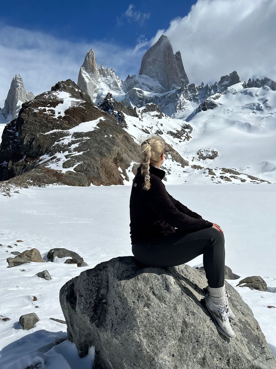 Person with braided hair sitting on a rock in snowy mountains, representing a one-way flight to Australia life change.