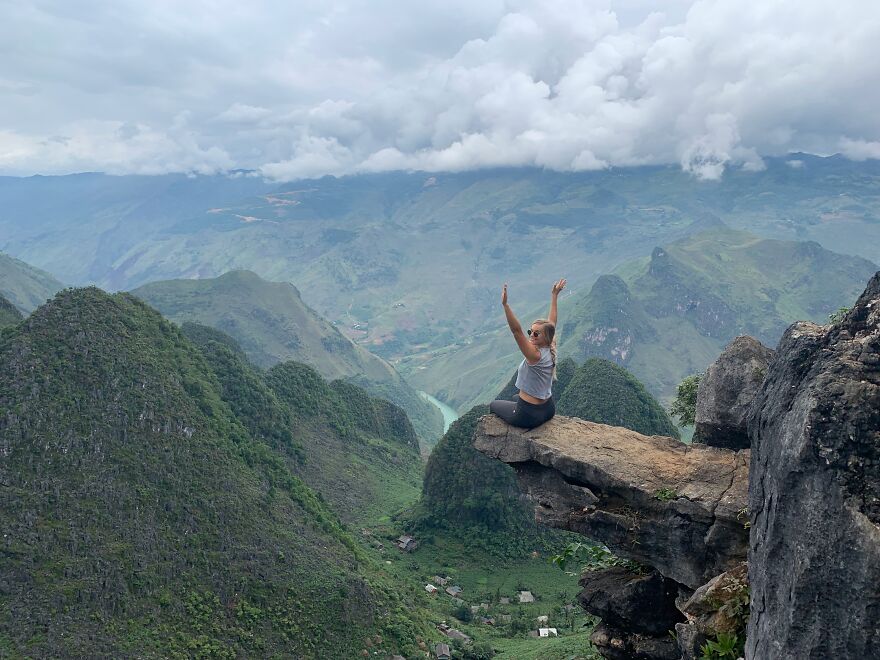 Person celebrating on a cliff edge overlooking mountains, symbolizing a new life after one-way flight to Australia and debt turnaround.