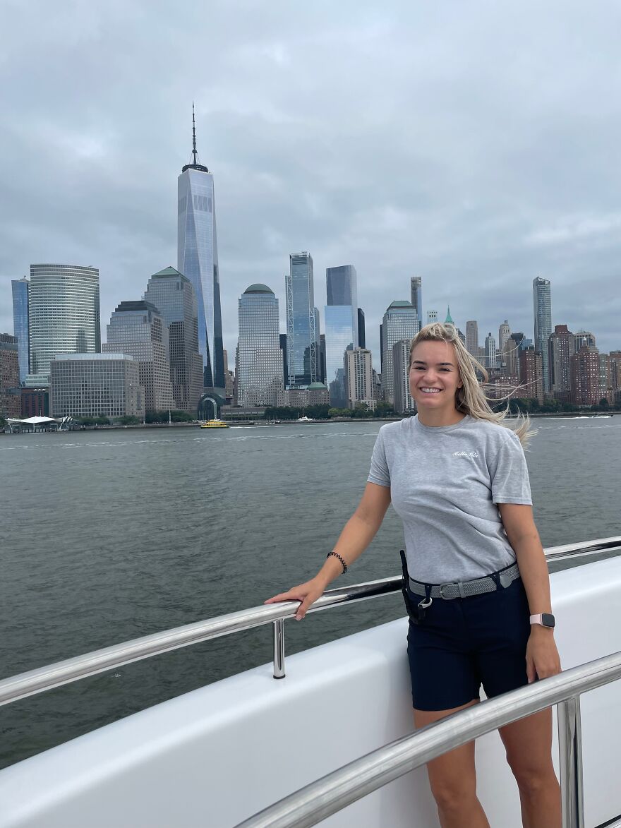 Young woman smiling on a boat with city skyline in background, symbolizing a one-way flight to Australia journey. Young woman smiling on a boat with city skyline in background, symbolizing a one-way flight to Australia journey.