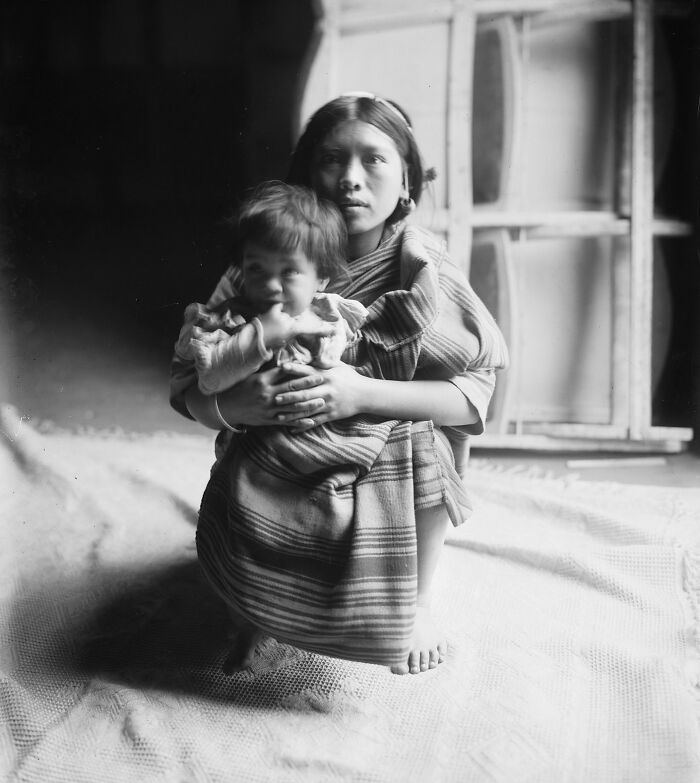 Young Filipino woman holding a child wrapped in traditional cloth, representing the Philippines in the 1890s contrasts.